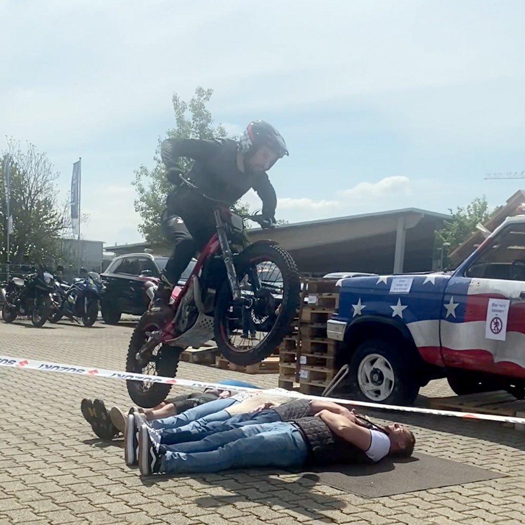 Ein junger Motorradfahrer springt mit seinem Fahrzeug über drei auf dem Boden liegenden Personen
