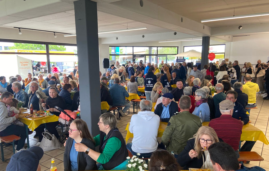Das Foto zeigt die eigentliche Ausstellungshalle, der Firma Autohaus Jauch in dem Frühlingsfesttische und Bänke aufgestellt sind. Dieser Ausstellungsraum ist voll besetzt mit Besuchern